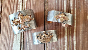 Three sterling silver cuff bracelets by Heather Elizabeth, one with crown, one with bee, one with fleur de lis